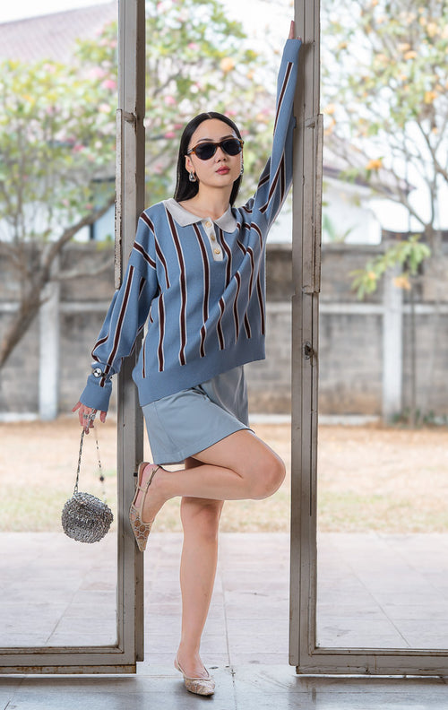 Sweater rajut wanita lengan panjang warna biru muda dengan detail garis vertikal kontras (light blue pinstripe polo knit sweater), kerah polo putih kontras (contrast white polo collar), dan penutup kancing depan (front-button closure).