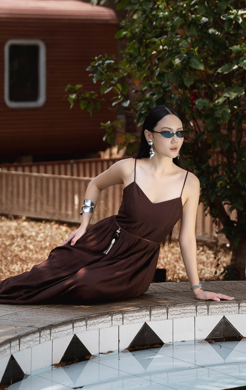 Dress panjang wanita warna cokelat tua (dark brown camisole maxi dress) Daphne Dress dengan model V-neck, tali bahu dapat disesuaikan (adjustable straps), serta bahan campuran katun poliester berstruktur dengan kerut elastis di bagian belakang. 
