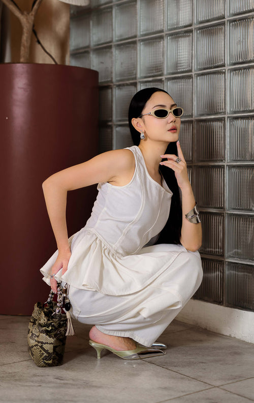 Blouse denim wanita warna putih (white denim peplum blouse) Emalyne Top dengan siluet feminin terstruktur (polished feminine silhouette), potongan pinggang turun yang tegas (defined drop-waist), peplum mengembang lembut (softly flared peplum), dan ritsleting belakang (back-zip closure).