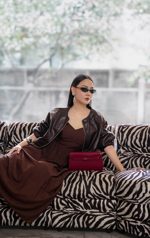 Jaket kulit wanita warna cokelat tua (dark brown leather jacket) Guinevere Jacket dengan lengan raglan santai (relaxed raglan sleeves), ritsleting depan (front zipper), saku fungsional, dan kelim karet elastis (stretch hem).