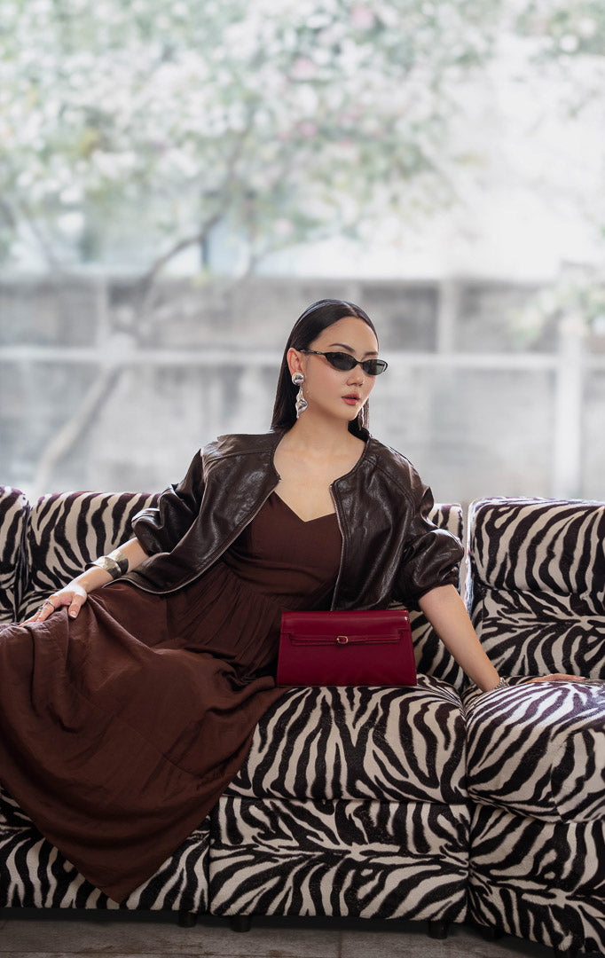Jaket kulit wanita warna cokelat tua (dark brown leather jacket) Guinevere Jacket dengan lengan raglan santai (relaxed raglan sleeves), ritsleting depan (front zipper), saku fungsional, dan kelim karet elastis (stretch hem).