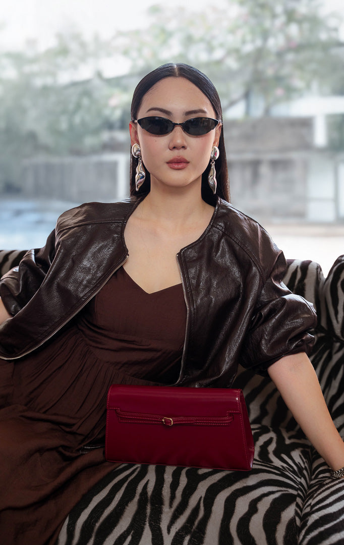 Jaket kulit wanita warna cokelat tua (dark brown leather jacket) Guinevere Jacket dengan lengan raglan santai (relaxed raglan sleeves), ritsleting depan (front zipper), saku fungsional, dan kelim karet elastis (stretch hem).