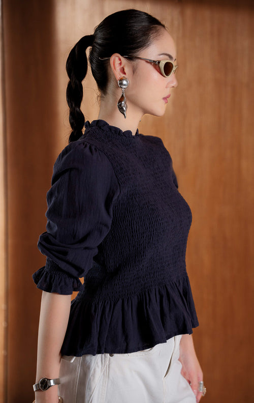 Blouse wanita lengan panjang warna navy (navy long sleeve blouse) Wynfield Top dengan bagian dada smock pas badan (flattering smocked bodice), siluet peplum mengembang lembut (softly flared peplum silhouette), serta bahan campuran katun linen bernapas (breathable cotton-linen blend).