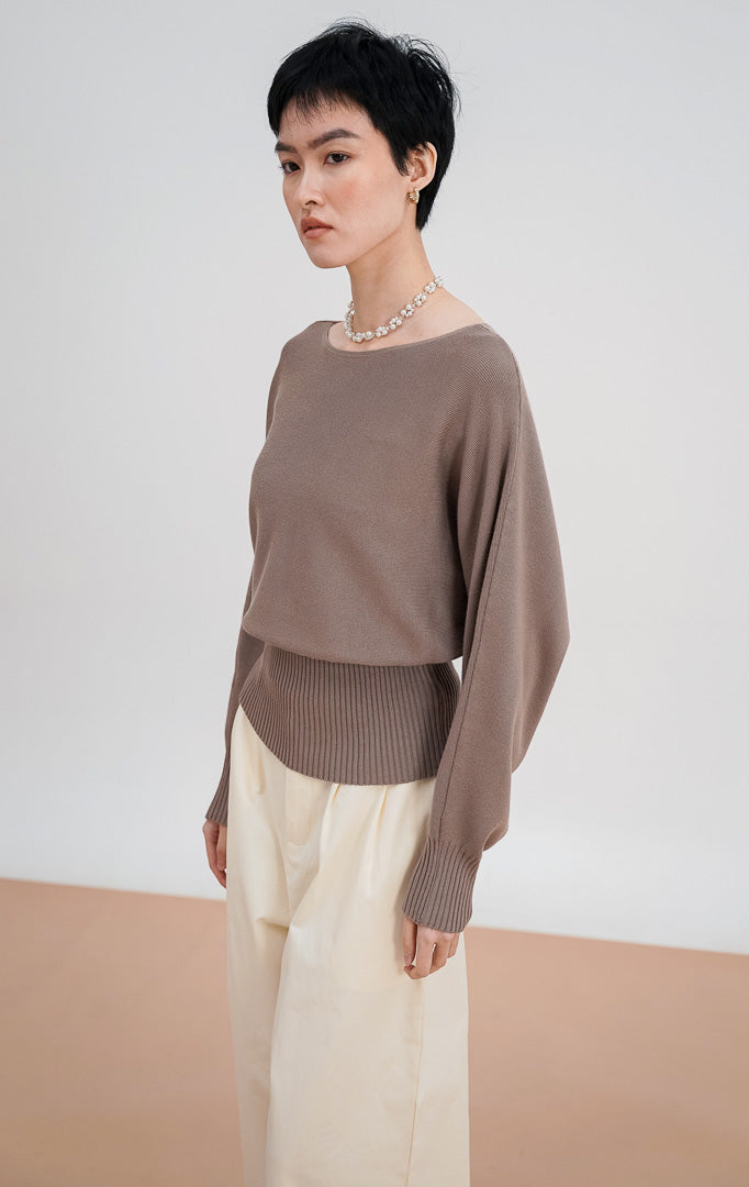 Model mengenakan Blair Sweater warna taupe, atasan rajut lengan panjang dengan potongan leher boat neck dan detail ban pinggang rajut lebar (ribbed waistband).