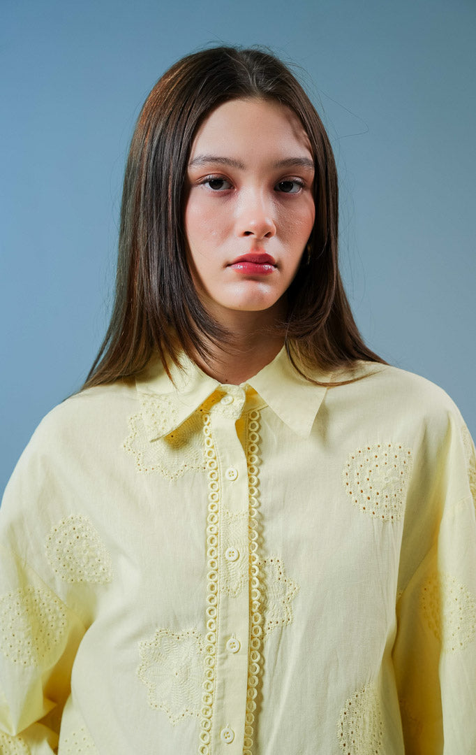 Model wanita mengenakan blouse Dimitry Embroidered Top warna butter yellow, kemeja katun wanita berkerah klasik dengan detail kancing depan dan bordir eyelet yang feminin. 