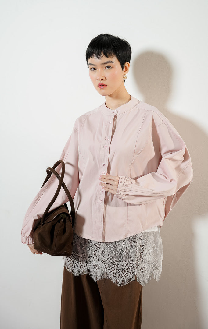 Model wanita mengenakan Rosemarie Round-Neck Twin Button Top warna light pink, atasan blouse kemeja wanita lengan balon warna merah muda dengan detail kancing ganda depan. 