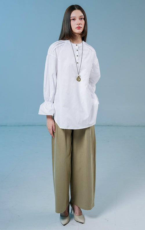 Model wanita mengenakan Cayden Long Sleeve Blouse warna putih, atasan katun berkerah bulat dengan detail lengan panjang beraksen ruffle dan kancing emas di bagian depan. 