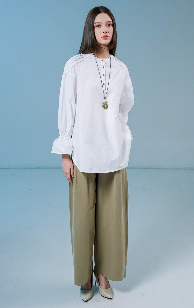 Model wanita mengenakan Cayden Long Sleeve Blouse warna putih, atasan katun berkerah bulat dengan detail lengan panjang beraksen ruffle dan kancing emas di bagian depan. 