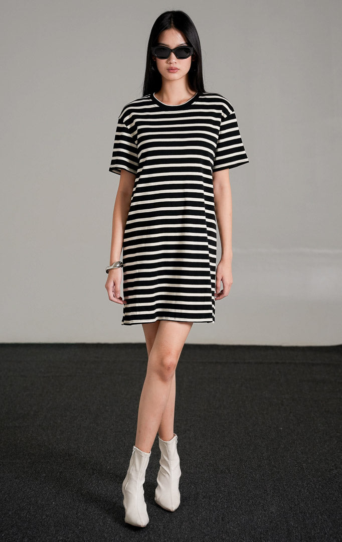 Breezy Striped Knit Dress, sebuah t-shirt dress pendek lengan pendek bermotif garis horizontal hitam dan putih, dipadukan dengan sepatu boots putih.