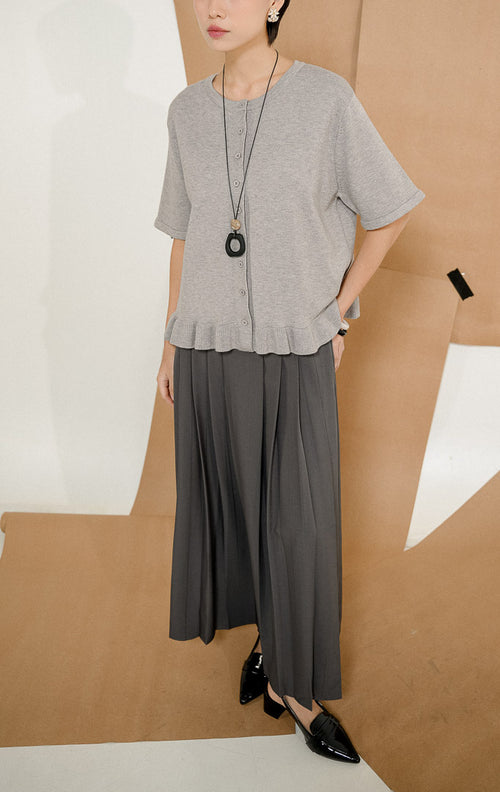 Model mengenakan Brinley Ruffle Hem Round Neck Top Grey, produk atasan rajut wanita lengan pendek warna abu-abu dengan kancing depan dan detail rempel. 