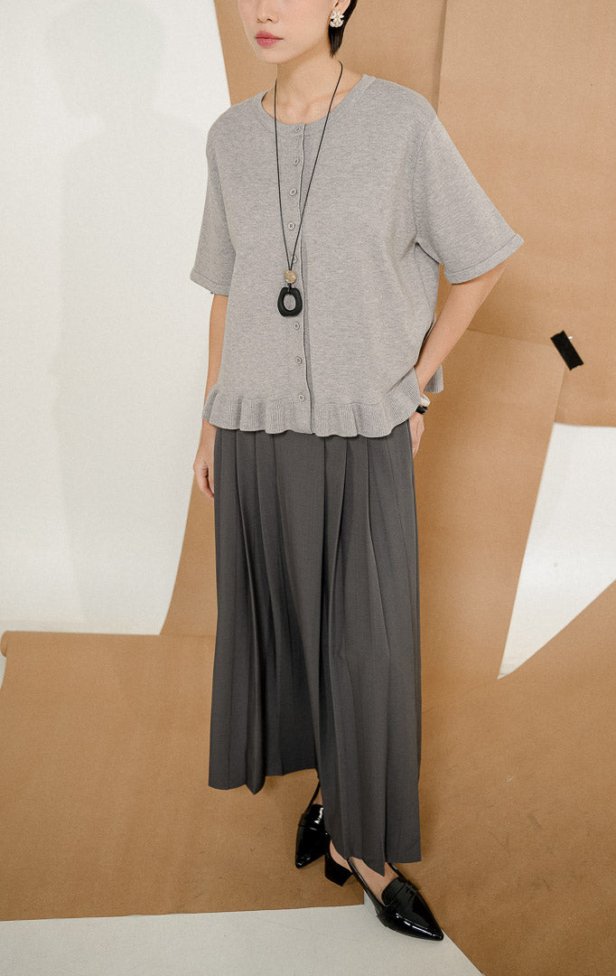 Model mengenakan Brinley Ruffle Hem Round Neck Top Grey, produk atasan rajut wanita lengan pendek warna abu-abu dengan kancing depan dan detail rempel. 
