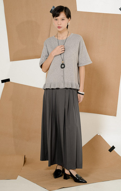 Model mengenakan Brinley Ruffle Hem Round Neck Top Grey, produk atasan rajut wanita lengan pendek warna abu-abu dengan kancing depan dan detail rempel. 