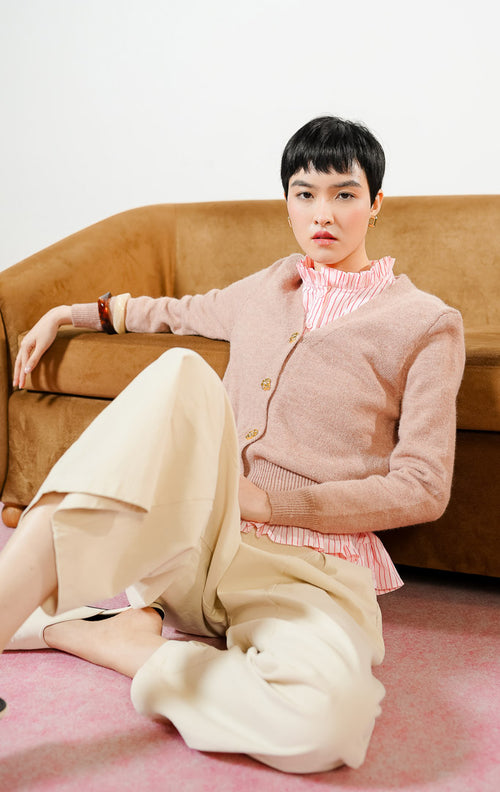 Model wanita bersandar di sofa mengenakan Yonna Cardigan warna dusty pink, atasan baju crop cardigan rajut bulu halus wanita leher V-neck dengan kancing emas mewah. 
