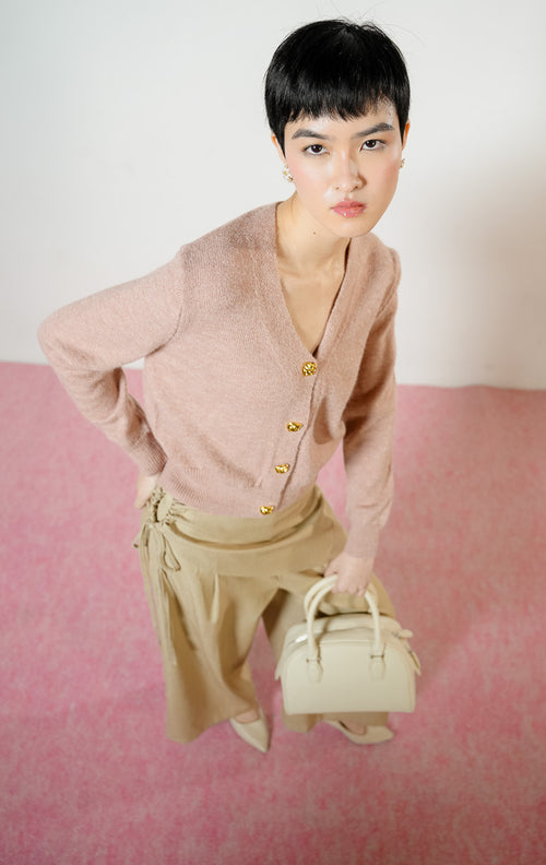 Model wanita bersandar di sofa mengenakan Yonna Cardigan warna dusty pink, atasan baju crop cardigan rajut bulu halus wanita leher V-neck dengan kancing emas mewah. 
