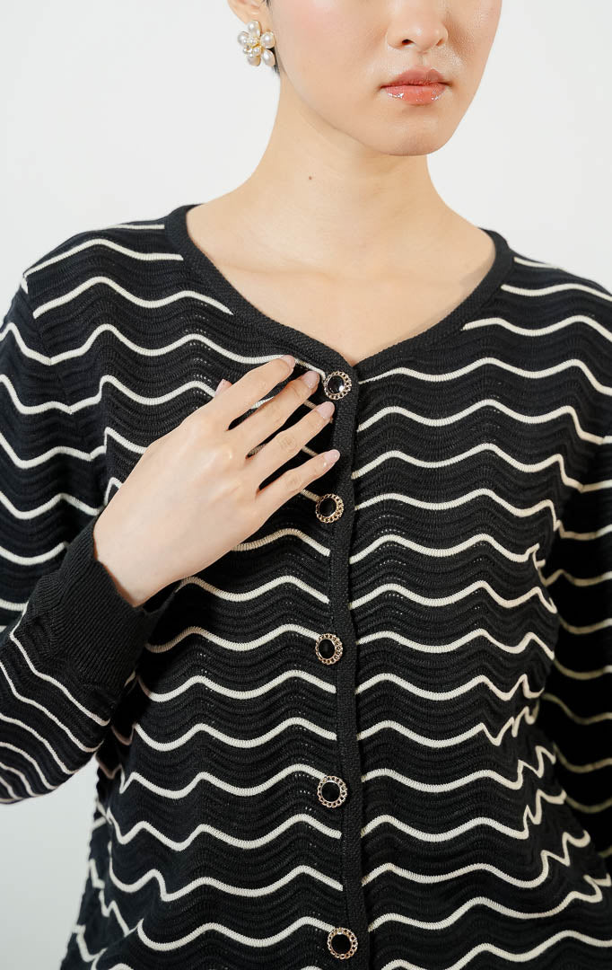 Model wanita mengenakan Aria Wavy Striped Knit Cardigan warna black, luaran cardigan rajut wanita lengan panjang berwarna hitam dengan motif garis bergelombang putih/krem unik. 
