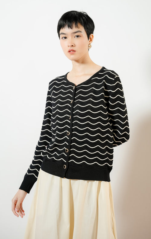 Model wanita mengenakan Aria Wavy Striped Knit Cardigan warna black, luaran cardigan rajut wanita lengan panjang berwarna hitam dengan motif garis bergelombang putih/krem unik. 