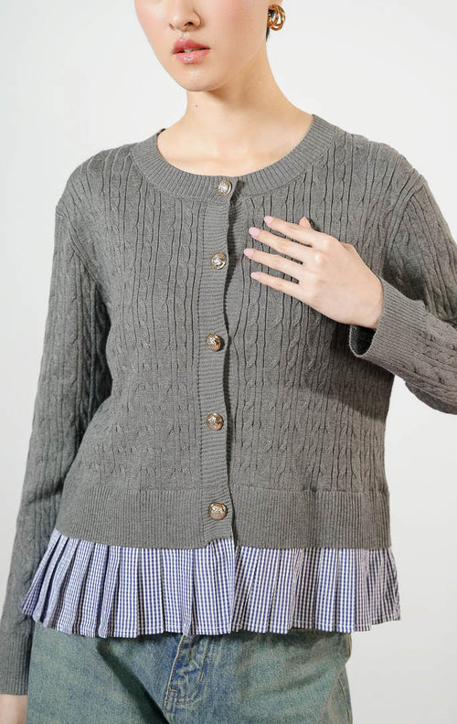 Model wanita mengenakan Malora Ruffled Flannel Hem Braided Knit Cardigan warna grey, outer cardigan rajut wanita motif kepang warna abu-abu dengan variasi kelim lipit kotak-kotak gingham biru dan kancing emas. 