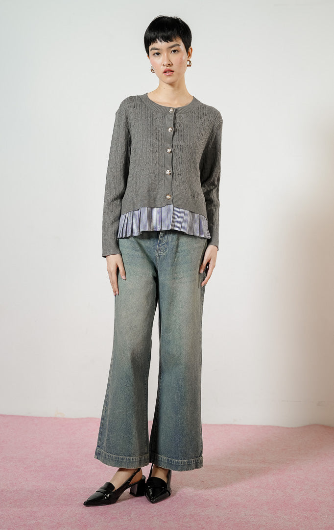 Model wanita mengenakan Malora Ruffled Flannel Hem Braided Knit Cardigan warna grey, outer cardigan rajut wanita motif kepang warna abu-abu dengan variasi kelim lipit kotak-kotak gingham biru dan kancing emas. 