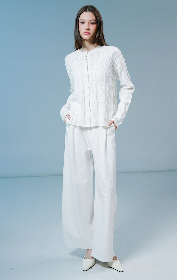 Model wanita mengenakan Twyla Textured Crew Neck Button-Up Cardigan warna white, luaran cardigan rajut wanita lengan panjang berwarna putih bersih dengan tekstur vertikal dan kancing depan. 
