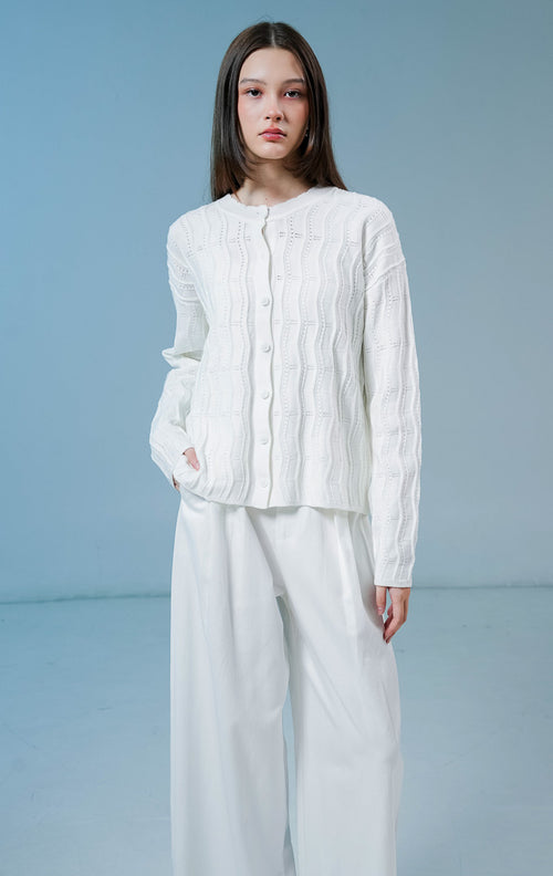 Model wanita mengenakan Twyla Textured Crew Neck Button-Up Cardigan warna white, luaran cardigan rajut wanita lengan panjang berwarna putih bersih dengan tekstur vertikal dan kancing depan. 