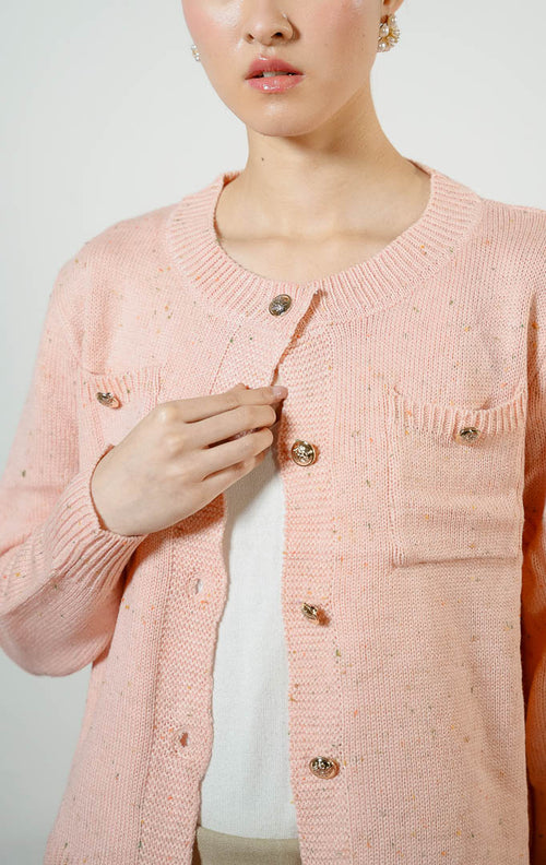 Model wanita mengenakan Chrystelle Gold Button Tweed Knit Cardigan warna pink, luaran kemeja cardigan rajut wanita bertekstur tweed warna merah muda dengan kancing emas mewah dan dua saku depan. 