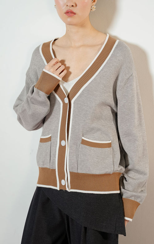Model wanita mengenakan Montclair V-Neck Contrast Rib Knit Cardigan warna grey, baju outer cardigan rajut wanita leher V warna abu-abu muda dengan detail karet rib kontras warna cokelat ala preppy varsity. 