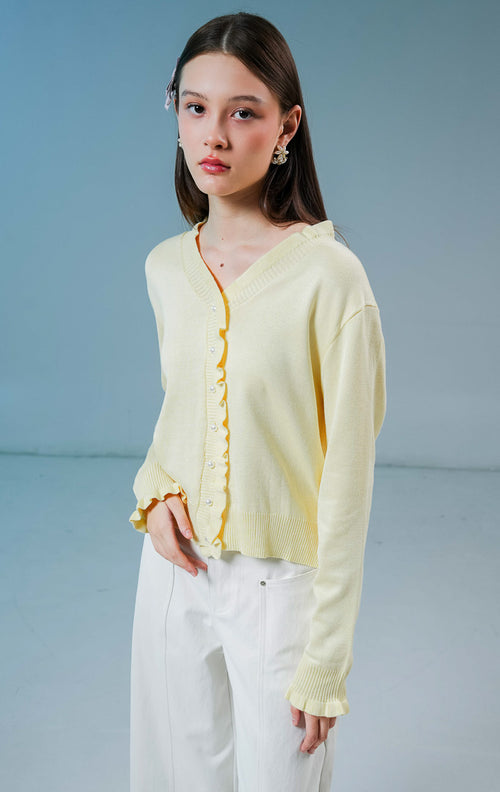 Model wanita mengenakan Graciella Ruffle Knit Cardigan warna butter yellow, luaran rajut wanita berkerah V dengan detail kerutan (ruffles) yang feminin dan kancing mutiara depan. 