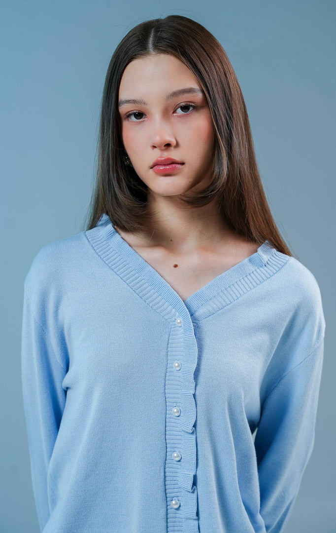 Model wanita mengenakan Graciella Ruffle Knit Cardigan warna light blue, luaran rajut wanita berkerah V dengan detail kerutan (ruffles) yang feminin dan kancing mutiara depan 