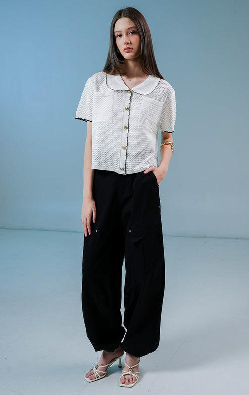 Model wanita mengenakan Mylah Pockets Knit Cardigan warna white, luaran cardigan rajut wanita lengan pendek berwarna putih dengan detail kerah bulat, tepian hitam, dan kancing emas. 