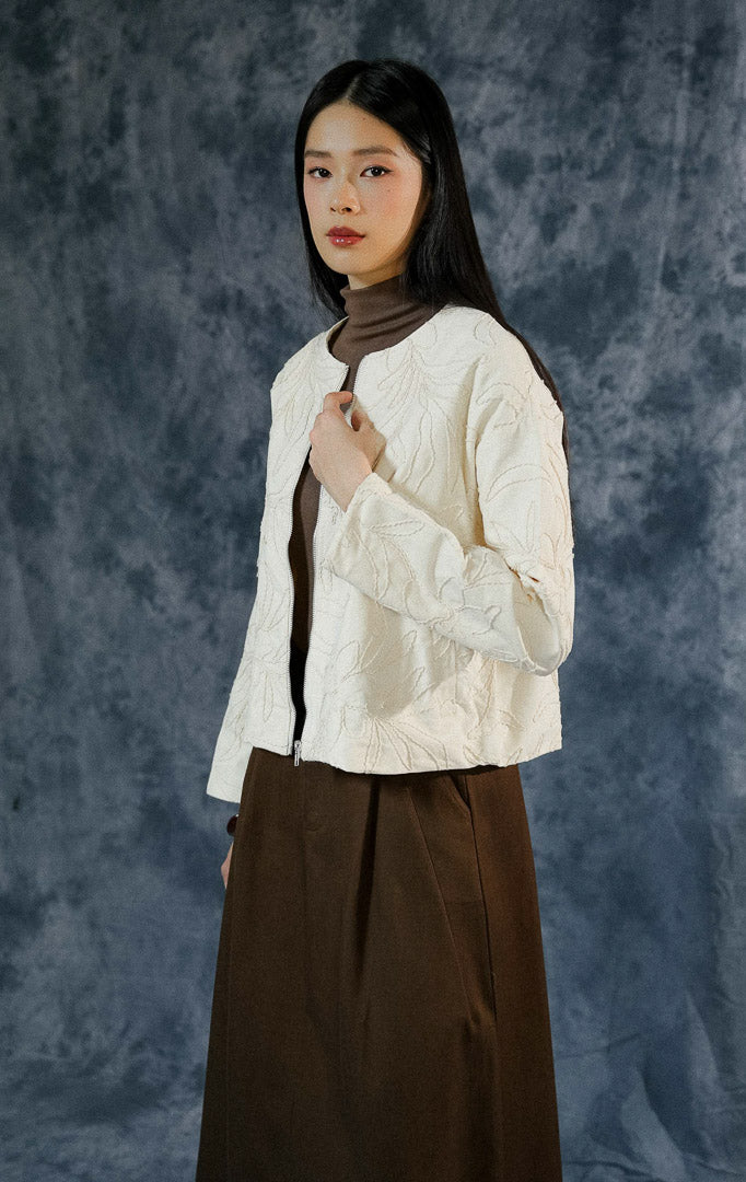 Atasan jaket lengan panjang wanita Catharina warna ivory berdesain Korean style, dilengkapi saku samping aktif dan detail bordir bunga estetik.