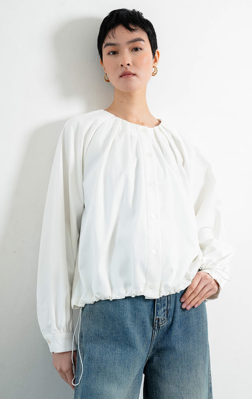 Atasan wanita lengan panjang warna putih (white) Catharine Top berbahan katun twill (cotton twill) dengan kerah bulat, bukaan kancing depan, dan detail tali serut di bagian bawah (drawstring hem). 