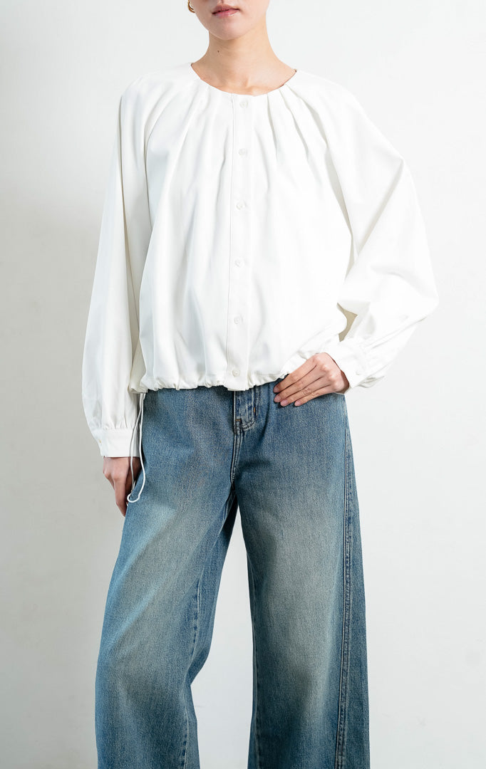 Atasan wanita lengan panjang warna putih (white) Catharine Top berbahan katun twill (cotton twill) dengan kerah bulat, bukaan kancing depan, dan detail tali serut di bagian bawah (drawstring hem). 