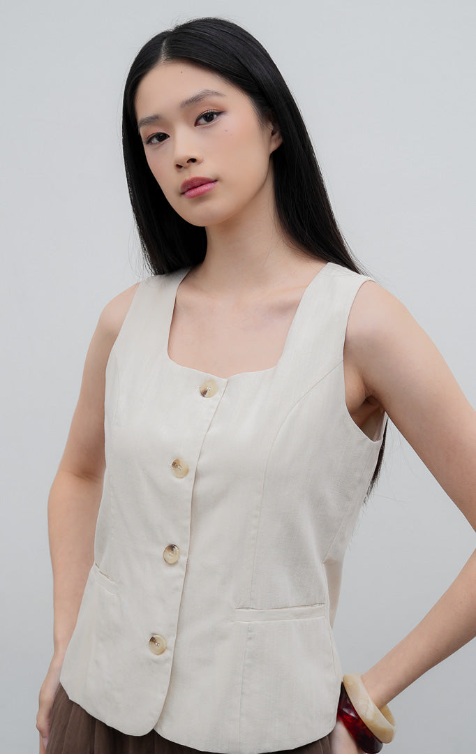 Rompi (vest) wanita tanpa lengan warna krem muda (ivory) Cedrica Vest dengan leher kotak (square neckline), kancing depan, dan detail aksen saku dekoratif.