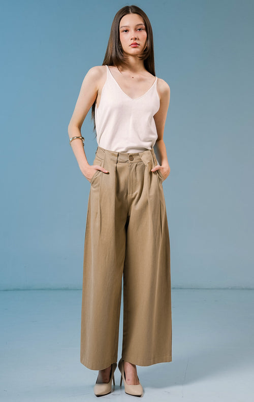 Model wanita mengenakan Normandy Pleated Straight Pants warna khaki, celana panjang bahan katun wanita dengan detail lipit depan dan potongan straight-leg. 