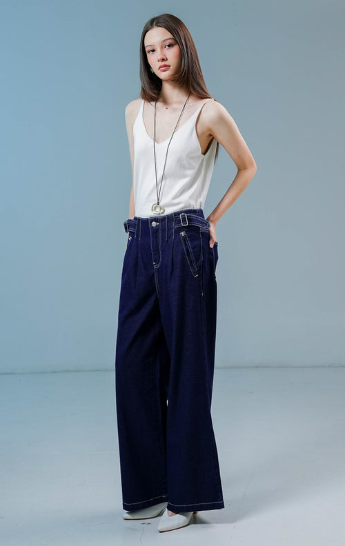 Model wanita mengenakan Luneth Pants warna dark denim, celana panjang kulot jeans wanita berpotongan longgar dengan detail lipit depan dan gesper samping unik. 