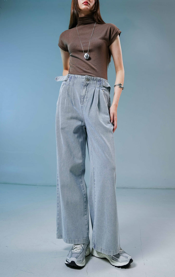 Model wanita mengenakan Luneth Pants warna light denim, celana panjang kulot jeans wanita berwarna biru muda dengan detail lipit depan dan gesper samping unik.