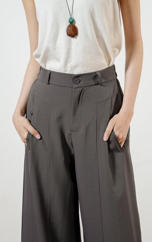 Model wanita mengenakan Earhart Inverted Pleat Wide Leg Pants warna grey, celana panjang kulot bahan poliester wanita berwarna abu-abu gelap dengan detail lipit depan dan potongan kaki lebar. 