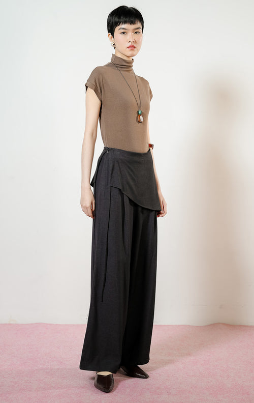 Model wanita mengenakan Nevon Side Tie Overlay Wide Leg Pants warna black, celana panjang kulot wanita berpotongan lebar warna hitam dengan detail lapisan asimetris unik di pinggang. 