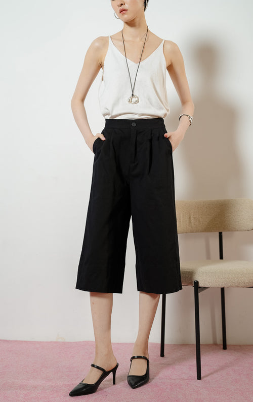 Model wanita duduk mengenakan Roderick Cropped Culottes Pants warna black, celana kulot gantung wanita bahan katun twill warna hitam dengan potongan sebetis. 