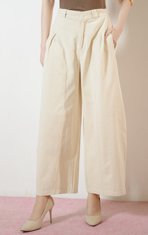 Model wanita mengenakan Regina Pants warna ivory, celana panjang kulot kerja wanita warna putih gading dengan potongan pinggang tinggi dan detail jahitan panel melengkung yang unik. 