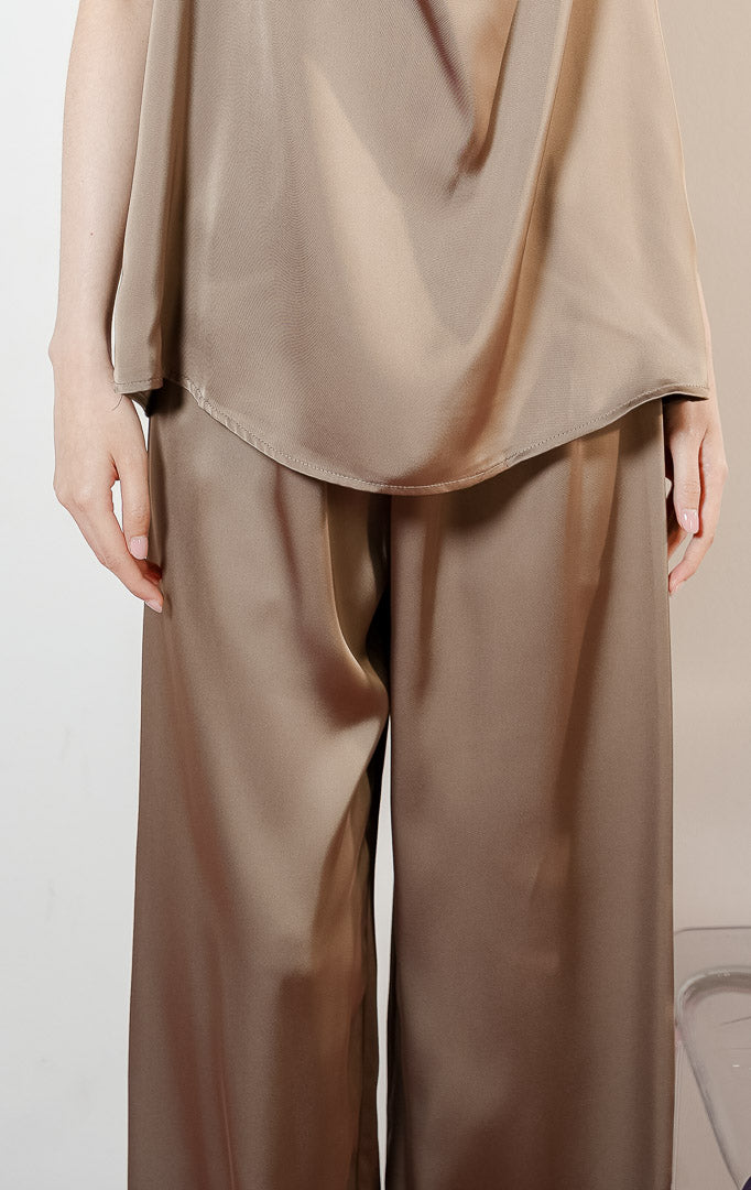 Detail bawahan model mengenakan Theodore Relaxed Satin Loose Pants warna taupe, celana panjang kulot wanita bahan satin mengkilap berwarna cokelat dengan pinggang karet. 