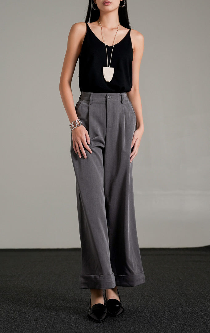 Celina Straight Pants warna abu-abu berpotongan lurus dengan detail lipatan di ujung celana, dipadukan dengan tank top hitam dan sepatu pantofel hitam.
