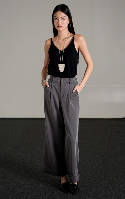 Celina Straight Pants warna abu-abu berpotongan lurus dengan detail lipatan di ujung celana, dipadukan dengan tank top hitam dan sepatu pantofel hitam.
