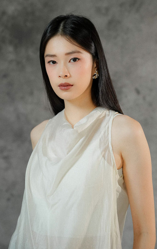 Atasan tanpa lengan wanita Charlette warna ivory dengan material poliester transparan (sheer finish) berdesain rapi dan kancing leher belakang.
