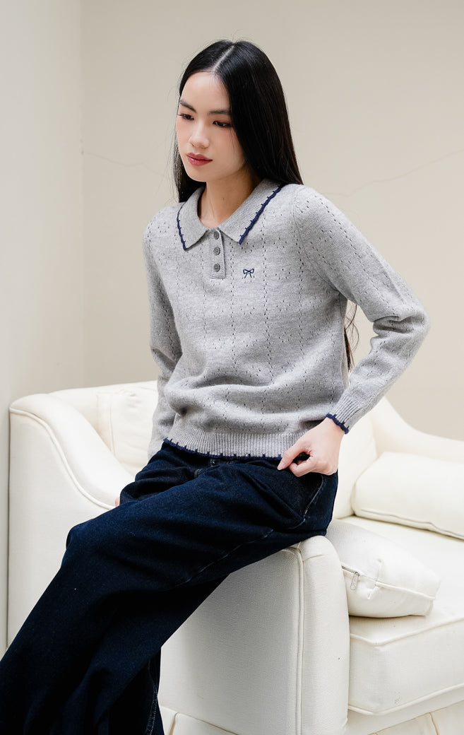Baju rajut wanita Chrystie Sweater warna grey (abu-abu) motif pointelle dengan detail kerah lis kontras navy, kancing depan, serta bordir pita yang feminine. 