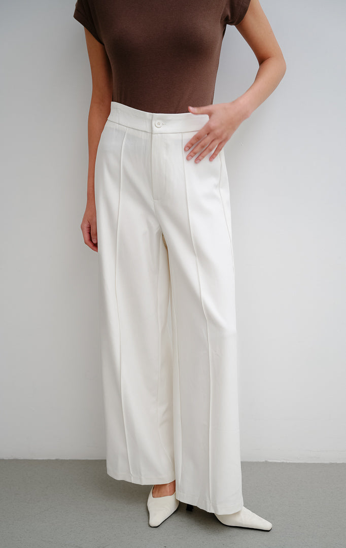 Celana panjang wanita warna putih Clarence Pants dengan potongan lurus (straight-cut), detail lipatan depan (front darts), dan pinggang karet bagian belakang.