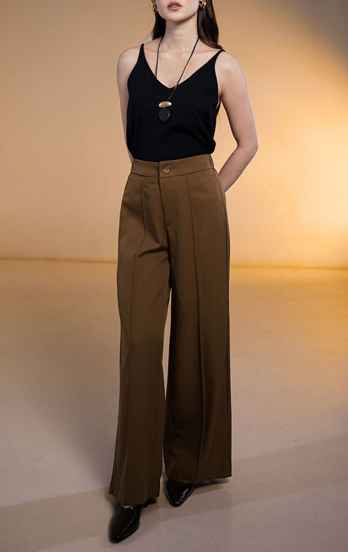Model wanita memakai Clarence Pants Dark Brown, celana panjang coklat tua potongan lurus dengan detail jahitan tulang depan (front darts) dipadukan dengan atasan tank top hitam