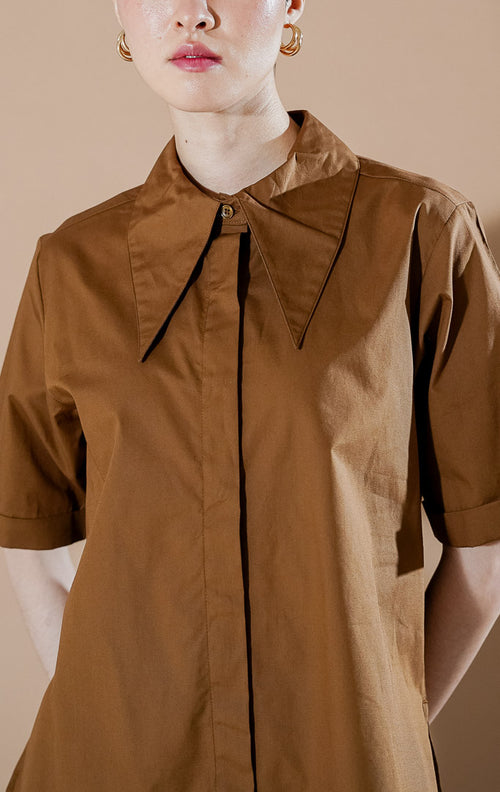 Model wanita mengenakan Cloudie Top Brown, kemeja lengan pendek berwarna cokelat dengan detail kerah lebar dan bahan katun yang berstruktur dari This Is April.