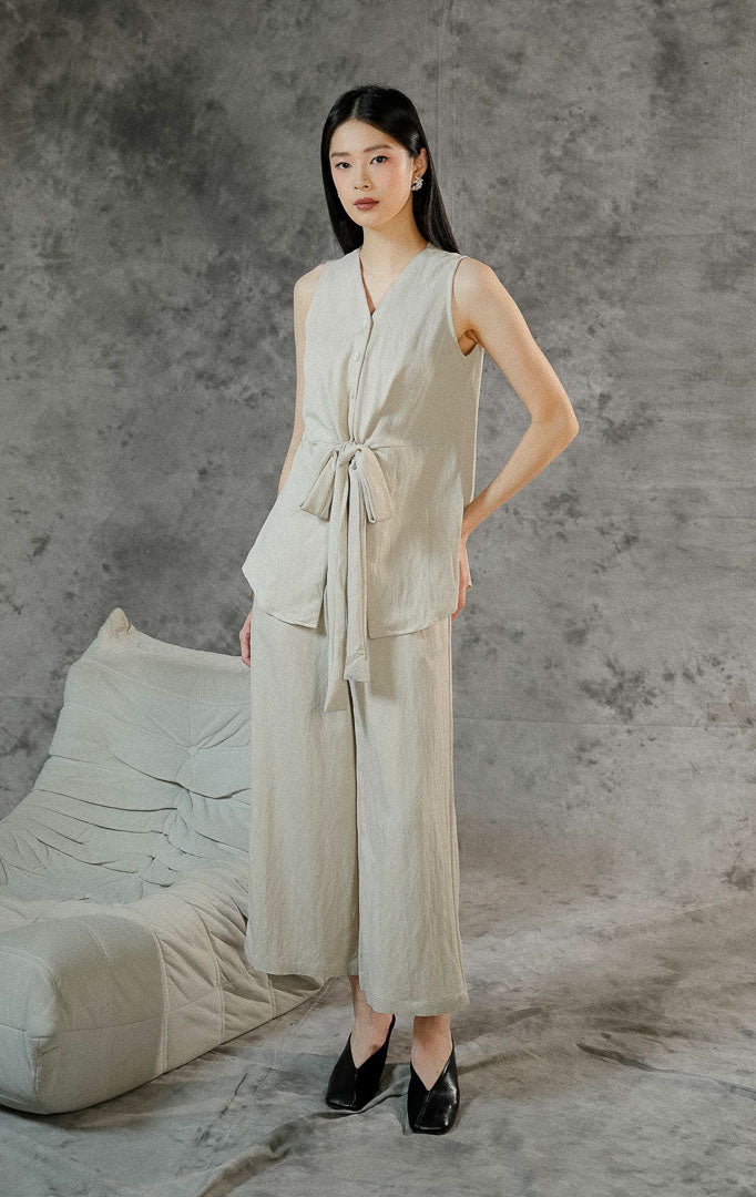 Setelan baju wanita Collette warna khaki polos terdiri dari atasan tanpa lengan dengan tali pita depan dan celana panjang dengan kancing resleting.
