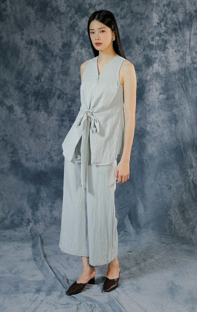 One set wanita berwarna light blue seri Collette, menampilkan atasan sleeveless berkerah rapi dengan detail tali serut pita aktif di pinggang depan.
